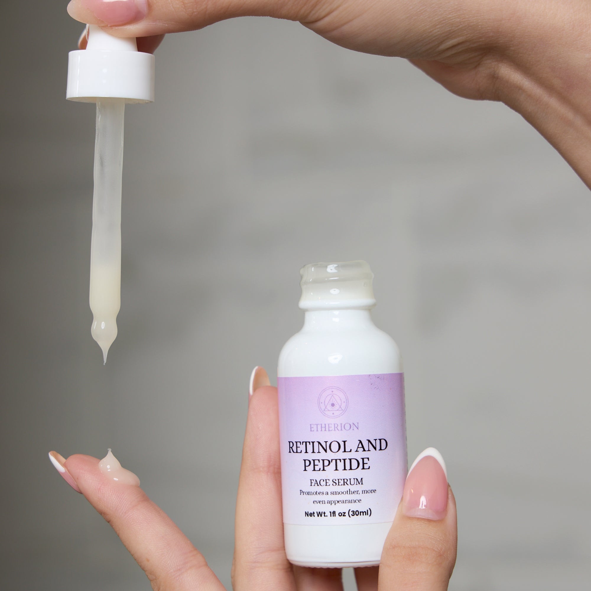 Hand holding a dropper and a bottle of Etherion Peptide Face Serum against a neutral background