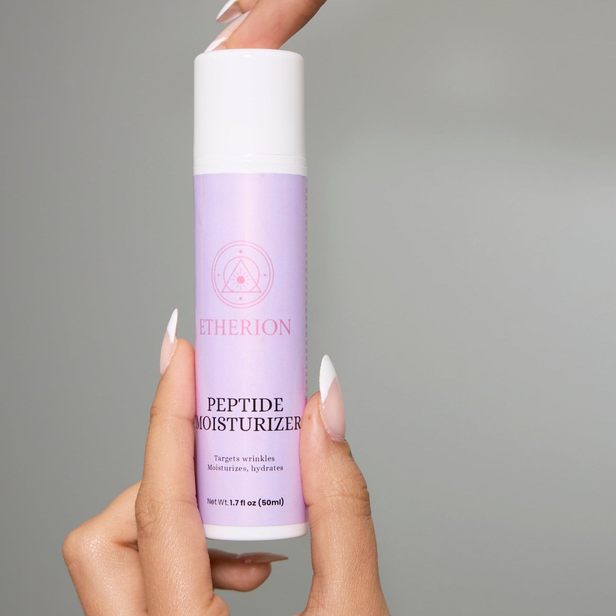 Hand holding a purple and white bottle of Etherion Peptide Moisturizer against a gray background